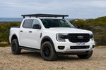 White Ford Ranger Next-Gen dual cab with black Roar 4x4 platform roof rack fitted, front three-quarter, coastal gravel